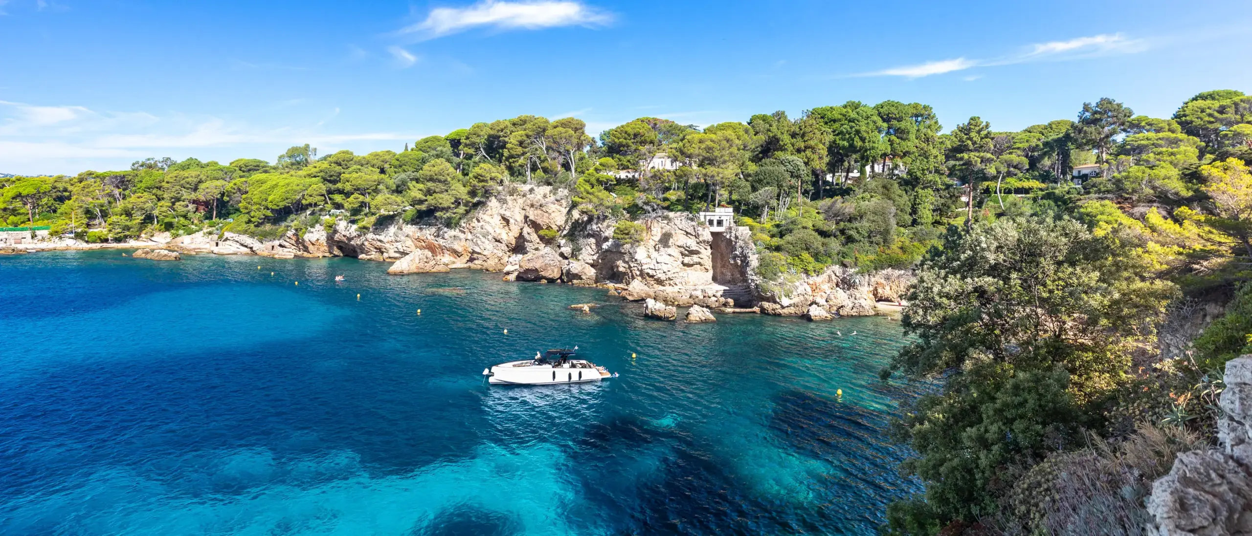 Ein Boot auf dem Wasser vor einer felsigen Küste mit grünen Bäumen.