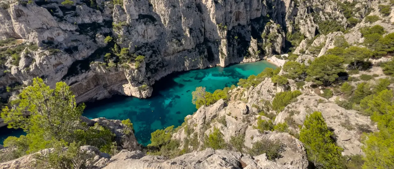 Ein türkisblauer See, umgeben von steilen Kalkstein Klippen und grünen Bäumen.