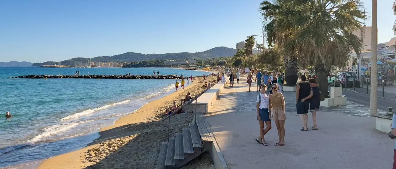 Ein Strand mit Menschen, die sich entspannen. Eine Promenade mit Palmen und Bänken.
