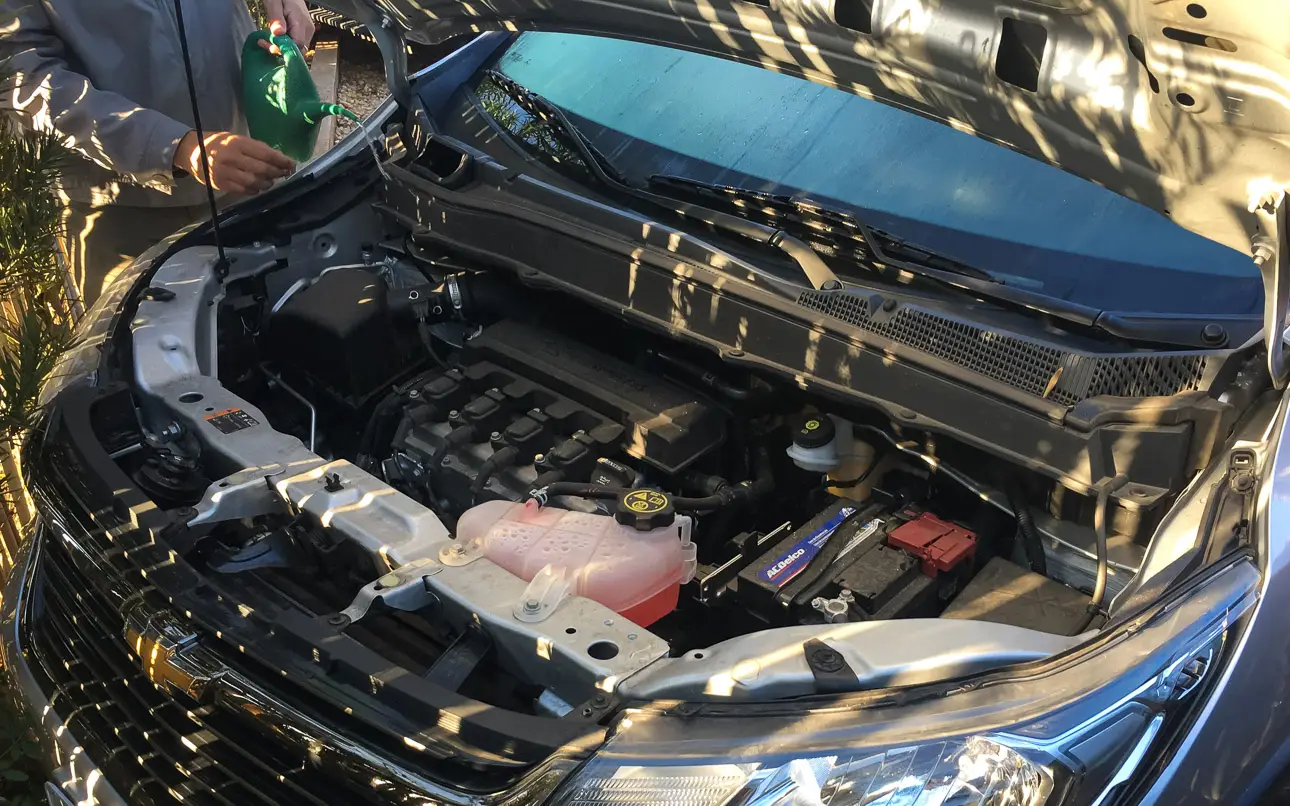 Motorraum eines Autos mit geöffneter Haube Ein Mann hält einen grünen Kanister, während er den Motorraum eines Autos überprüft.