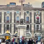 Eine Menschenmenge steht vor einem historischen Gebäude mit einer Statue in der Mitte. Das Gebäude hat eine beeindruckende Architektur.