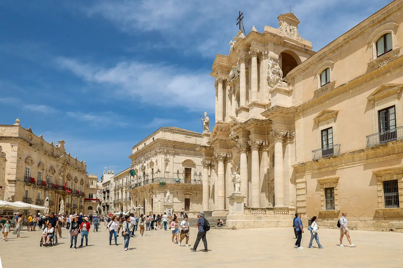 Ein großes Publikum auf einem Platz mit historischen Gebäuden. Der Himmel ist blau mit Wolken.
